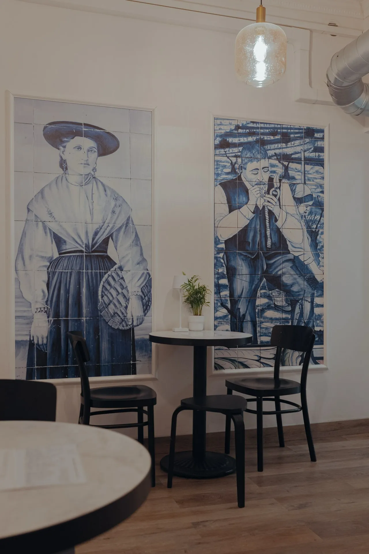 Dwa wysokie panele azulejos z postaciami w portugalskich strojach, pod nimi okrągły stolik i czarne krzesła w BOM DIA przy Sławkowskiej