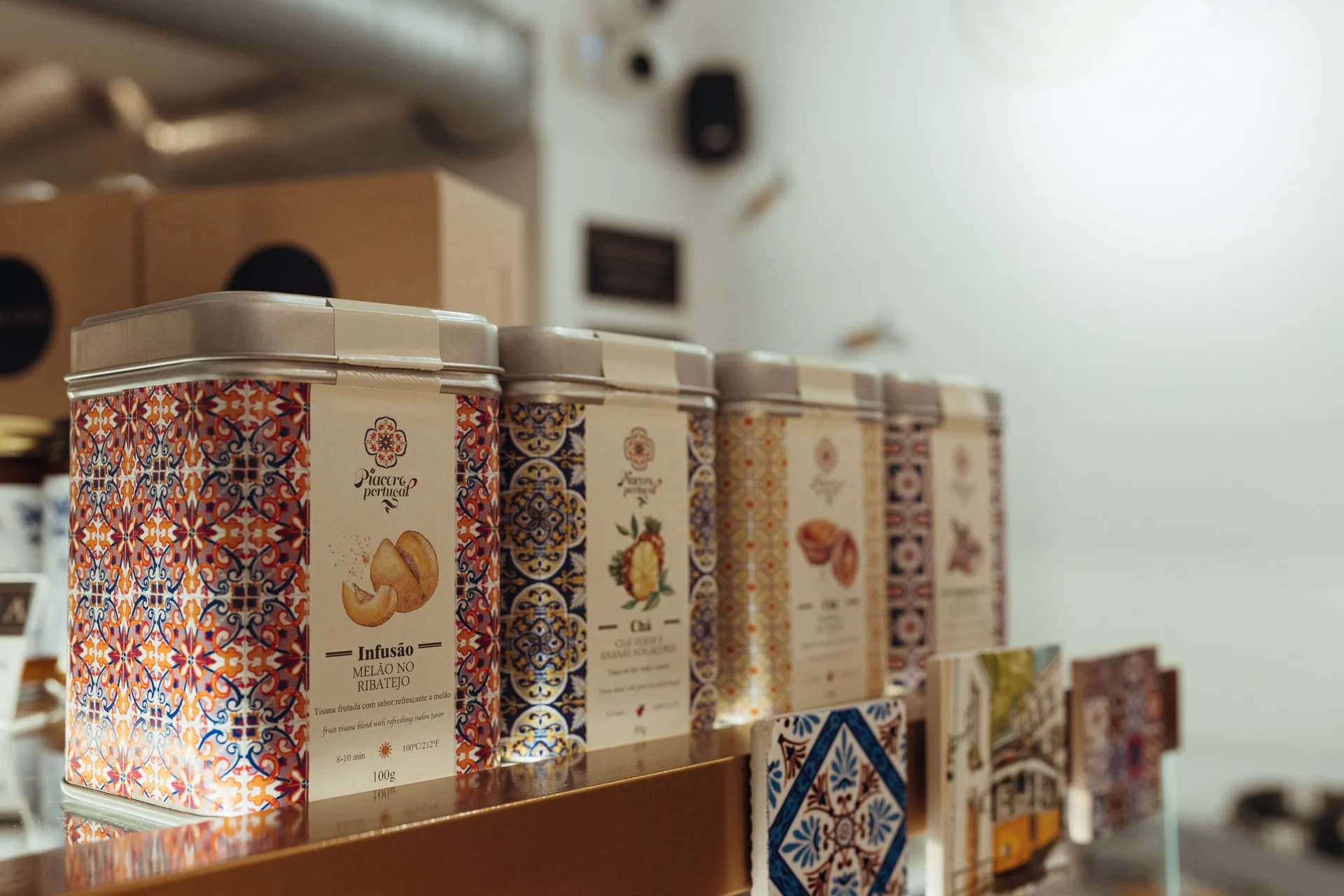 Ozdobne puszki portugalskich herbat we wzory azulejos na półce sklepiku, obok pocztówki