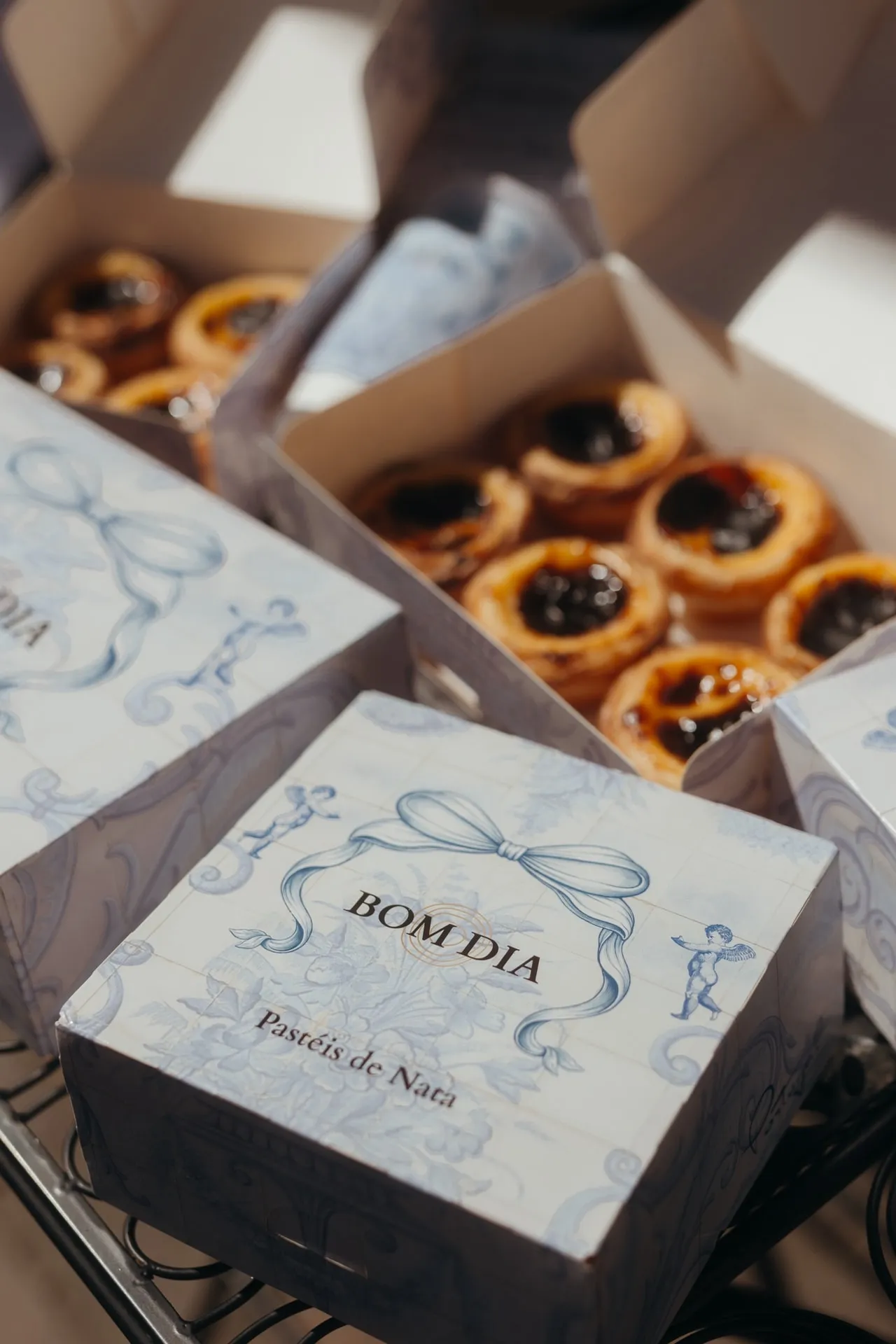 Pastéis de Nata w otwartych pudełkach BOM DIA, na pierwszym planie zamknięte pudełko z kokardą