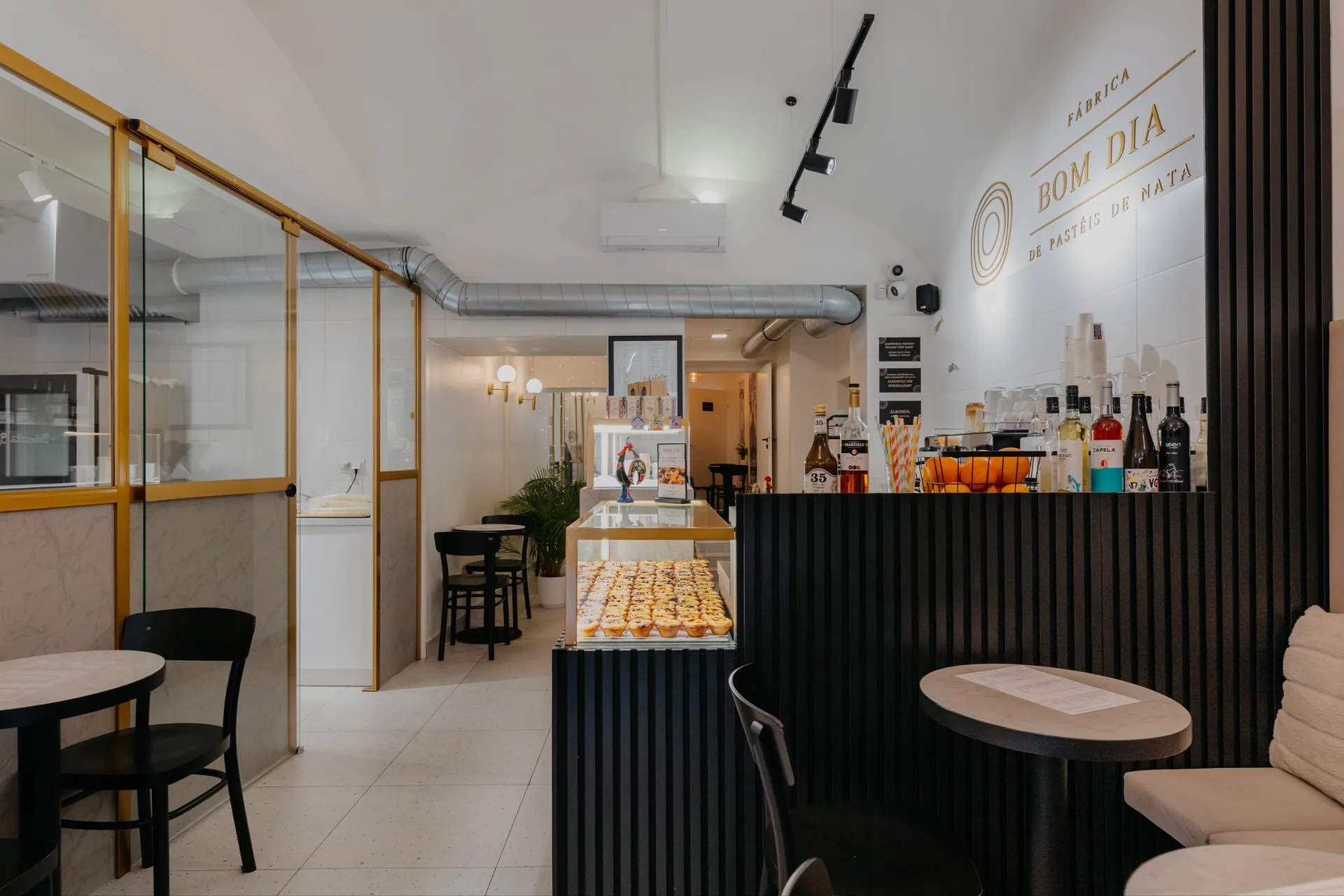 Wnętrze BOM DIA Fábrica de pastéis de nata przy Sławkowskiej: lada z Pastéis de Nata, stoliki i przeszklona pracownia
